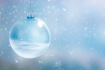 Transparente Glaskugel vor unscharfem Winterhintergrund mit Schneeflocken