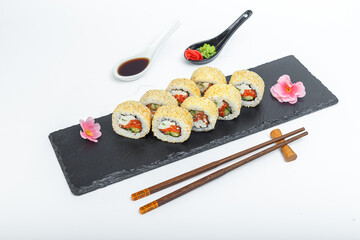 Roll Caesar with salmon and sesame, bowls and sticks, on a black plate, slate stand, on a white isolated background