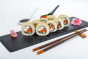 Roll Caesar with salmon and sesame, bowls and sticks, on a black plate, slate stand, on a white isolated background
