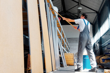 Professional industrial painter paints wooden boards with paint roller. Caucasian worker in overalls paints wooden surface indoors.