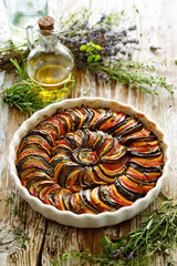 Ratatouille from sliced colorful vegetables in a baking dish on a wooden table, close-up view - obrazy, fototapety, plakaty