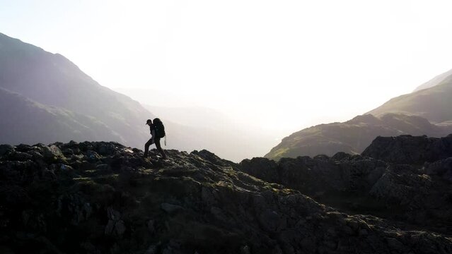 Aerial view of hiker on mountain, overlooking the valleys and lakes on a sunny day in the English Lake District National Park, United Kingdom. View of English Fells from mountain top.