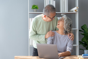 Happy mature couple using laptop at home. Happy elderly Asian couple laughing bonding together sitting at home table with laptop.