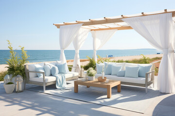 A coastal outdoor seating area with a white pergola, blue and white outdoor sofas, and potted plants and pillows.