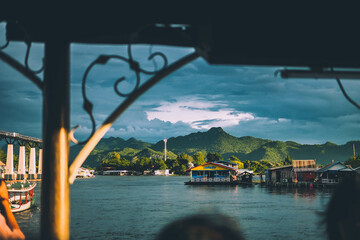Kanchanaburi, Thailand - September 11, 2022 : View of a raft boat floating in the River Kwai with a mountain in the background - obrazy, fototapety, plakaty