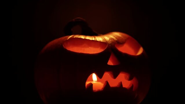 Close up hand carved art of smiling evil pumpkin jack o lantern for Halloween. Holiday celebration, spirits and demons autumn backdrop. Candle lights eyes glow. Infernal and mystical background.