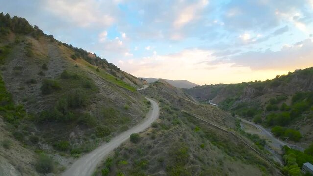 Drone soars above mountainous terrain, capturing winding roads and expansive grasslands, offering a breathtaking aerial view of the majestic landscape
