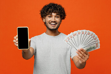 Young rich happy Indian man wear t-shirt casual clothes hold in hand fan of cash money in dollar...