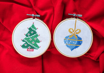 Details of handmade cross-stitch and wooden decoration for Christmas on red background.