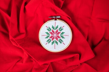 Details of handmade cross-stitch and wooden decoration for Christmas on red background.