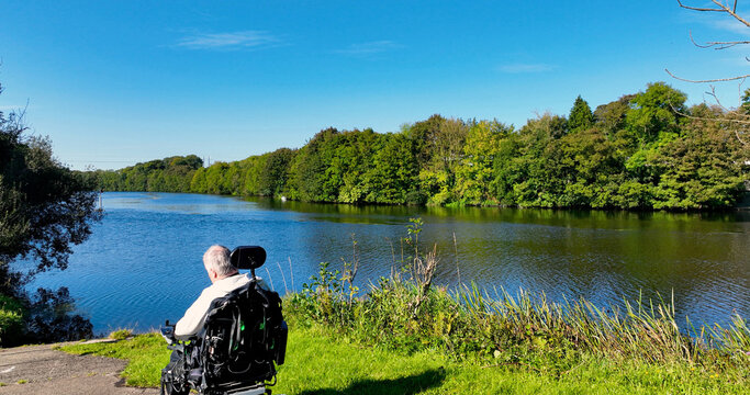 Disabled man in a wheelchair looking into river in the woods - Powered by Adobe