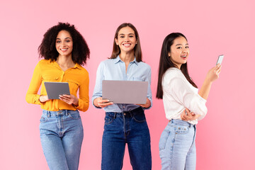People and technology concept. Happy diverse female friends using different gadgets laptop, tablet...