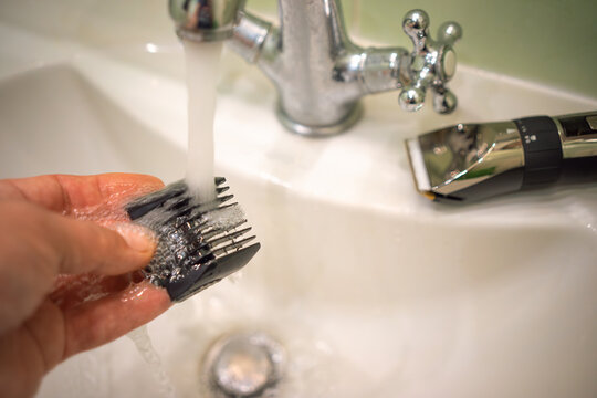 Washing the electric shaver nozzle under the tap.Disinfection of the barber's tool under a stream of water in the faucet. Cleaning the razor for cutting hair.