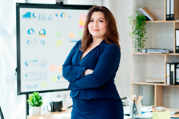 A plus size woman in a blue blouse and blue skirt stands in the office