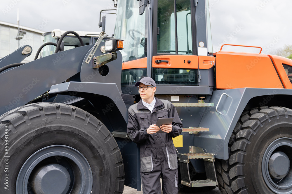 Poster Serviceman with digital tablet on a background of the tractor.