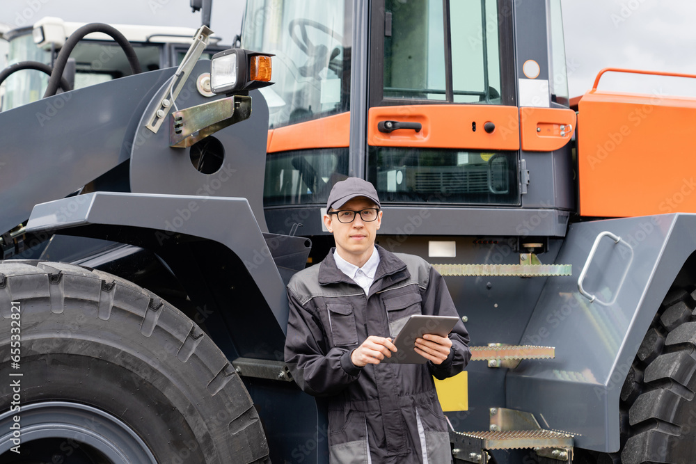 Poster serviceman with digital tablet on a background of the tractor.