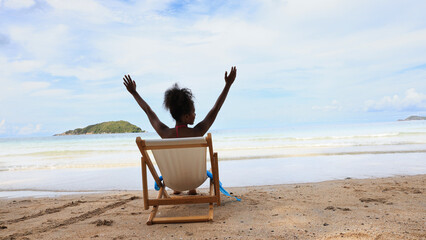 Enjoy Black woman sit relax on white sunchair on tropical beach 
