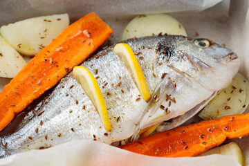 Marinated dorado fish with vegetables and spices on baking sheet before baking. Close up