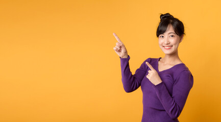 Beautiful young Asian woman 30s wearing purple shirt pointing up to copy space with smile face and...