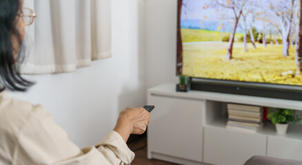Elderly woman Watching smart TV and using remote controller Hand holding television audio remote...