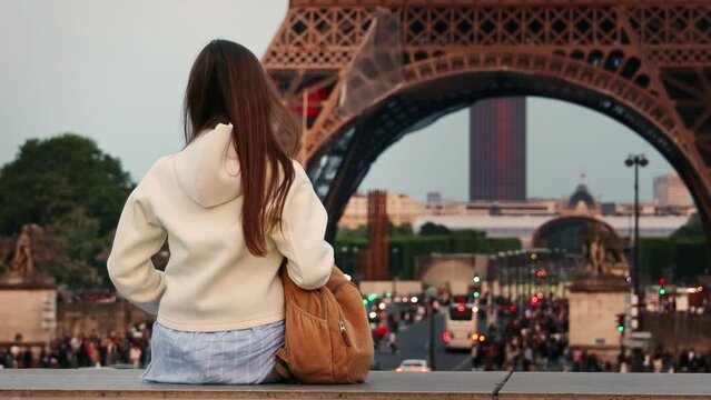 Young woman sitting in front of the Eiffel Tower.