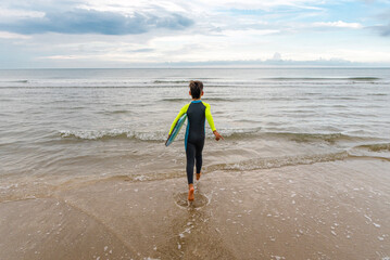 Young beach boy in a wet suit running or walking into the water while carrying his boogie board