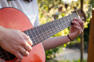 A girl plays an acoustic guitar in the garden. Close-up of female hands playing a classical guitar.  © jarizPJ