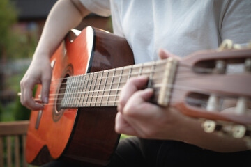 A girl plays an acoustic guitar in the garden. Close-up of female hands playing a classical guitar.
