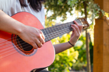 A girl plays an acoustic guitar in the garden. Close-up of female hands playing a classical guitar. 