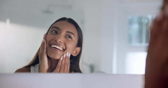 Woman, mirror and touch face with beauty in reflection in bathroom, skincare and wink with smile. Female person, indian and holding cheek with self love, home and natural beautiful with youth glow