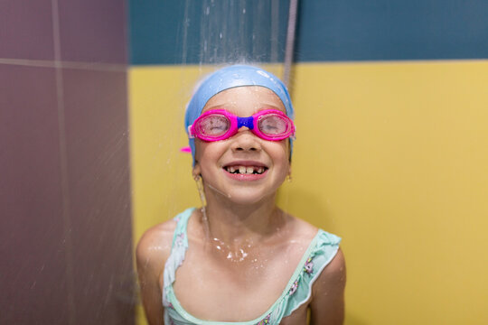 Child in swimsuit and goggles taking shower after workout in pool