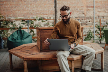 A stylish male freelancer is working on a new startup project, analyzing data using a laptop and a 5G wireless internet connection in a city cafe on a summer terrace with a free Wi-Fi zone - obrazy, fototapety, plakaty