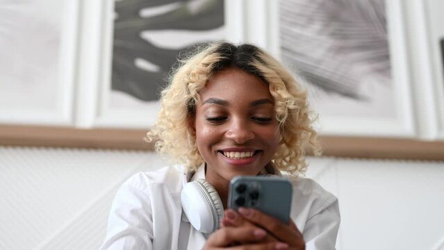 Happy dark skinned girl using smartphone for dating app,online shopping,messaging,watching videos