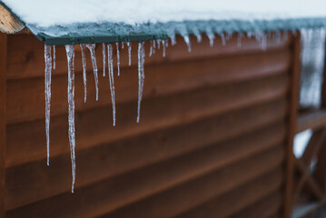 Icicles on the roof of a wooden house close-up. Sub-zero temperature, snowy weather, winter symbol snow and ice