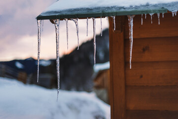 Icicles on the roof of a wooden house close-up. Sub-zero temperature, snowy weather, winter symbol snow and ice