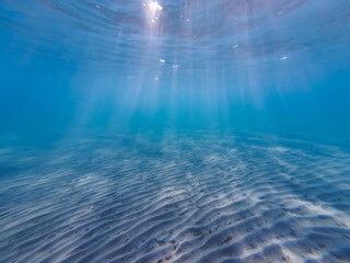 Sandy bottom on the beach in Greece, the sun's rays break through the water.  Underwater photo.