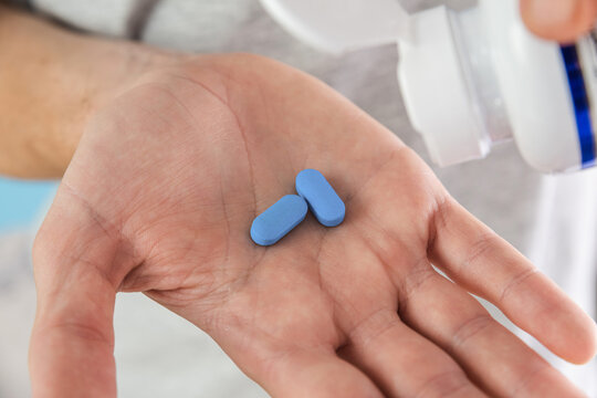 Man pouring a PrEP blue pill from medical bottle in a hand. HIV prevention using Pre-Exposure Prophylaxis medicine. Men health. AIDS prevention concept