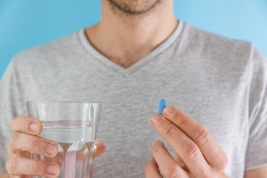 Man drinking a PrEP blue pill with glass of water. HIV prevention using Pre-Exposure Prophylaxis medicine. Men health. AIDS prevention concept
