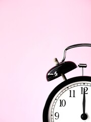 Black retro alarm clock at 12 twelve o clock on a pink bakground with copy space to add text 12am...