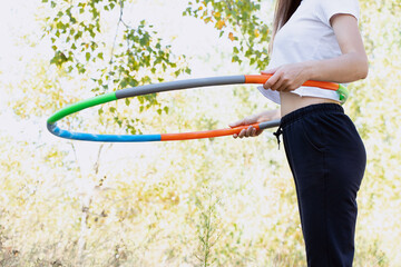 In the summer in a park in Ukraine, a young woman with a sports hoop on her waist does fitness with a hoop and maintains her figure © Виктория Котлярчук