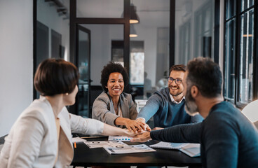 An interracial group of happy businesspeople is stacking hands for teamwork at the office.