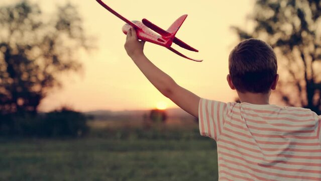 Child aviator. Boy wants to become pilot, astronaut. Slow motion. Happy kid runs with toy airplane on field in sunset light. Children play toy airplane. Teenager dreams of flying and becoming pilot.