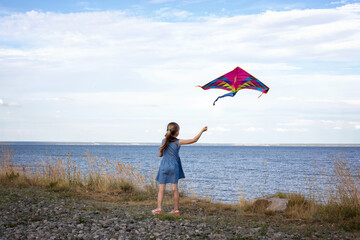 Little girl playing with flying kite on the coast. Kite flying in the wind. The child plays outdoors in the beach.