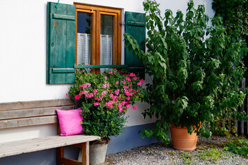 Fototapeta na wymiar romantic traditional alpine Bavarian farmhouse with geraniums on window ledge, wooden bench with pink pillow and lush tree, Schwangau, Bavaria 