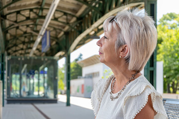 Elderly woman 60-65 years old at a bus stop waiting for a train or train