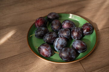 Fresh purple ripe plums on a green plate, close-up. Harvest. Fiber