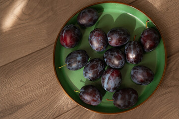 Fresh purple ripe plums on a green plate, close-up. Harvest. Fiber