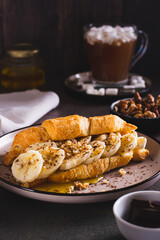 Delicious croissant with banana, honey, chocolate and nuts on a plate on the table vertical view