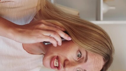 Vertical video. Unhappy call. Mobile phone talking. Disturbed worried woman arguing on smartphone unpleasant communication in light room interior.