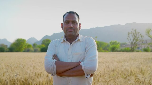 A happy Indian man or male farmer is standing with folded hands or crossed arms looking or facing the camera smiling on an agricultural farm or field in a rural village. Agriculture concept